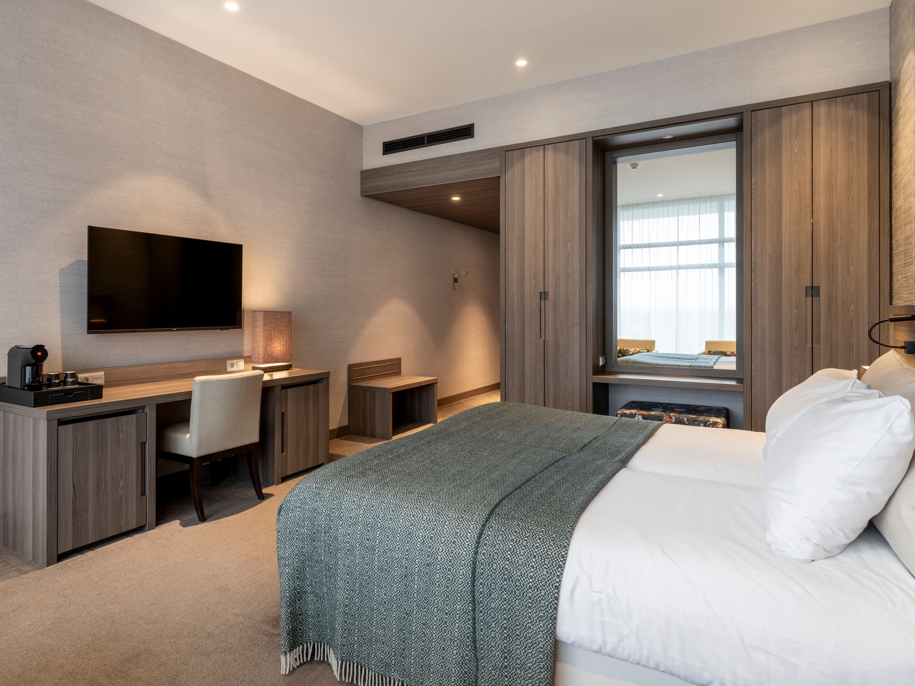 Una habitación de hotel moderna con una cama, un escritorio, una silla, un televisor y un armario.