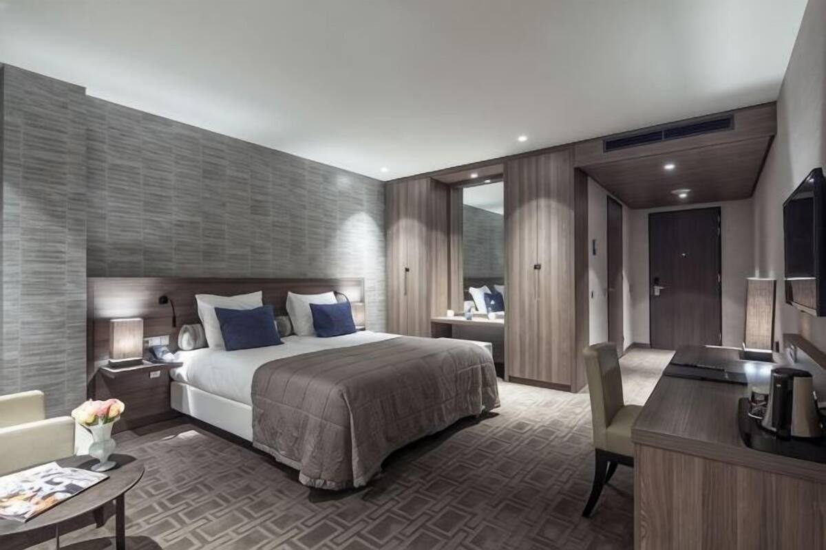 A modern hotel room with a large bed, bedside tables, a desk, and a mirror.