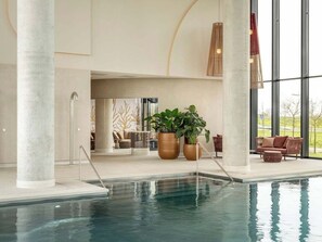 An indoor swimming pool with clear glass walls, large potted plants, and a modern interior design. - Van der Valk Hotel Zwolle (Zwolle)
