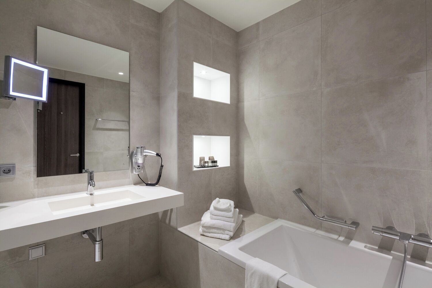 A modern bathroom with a large mirror, a sink, a bathtub, and a towel rack.