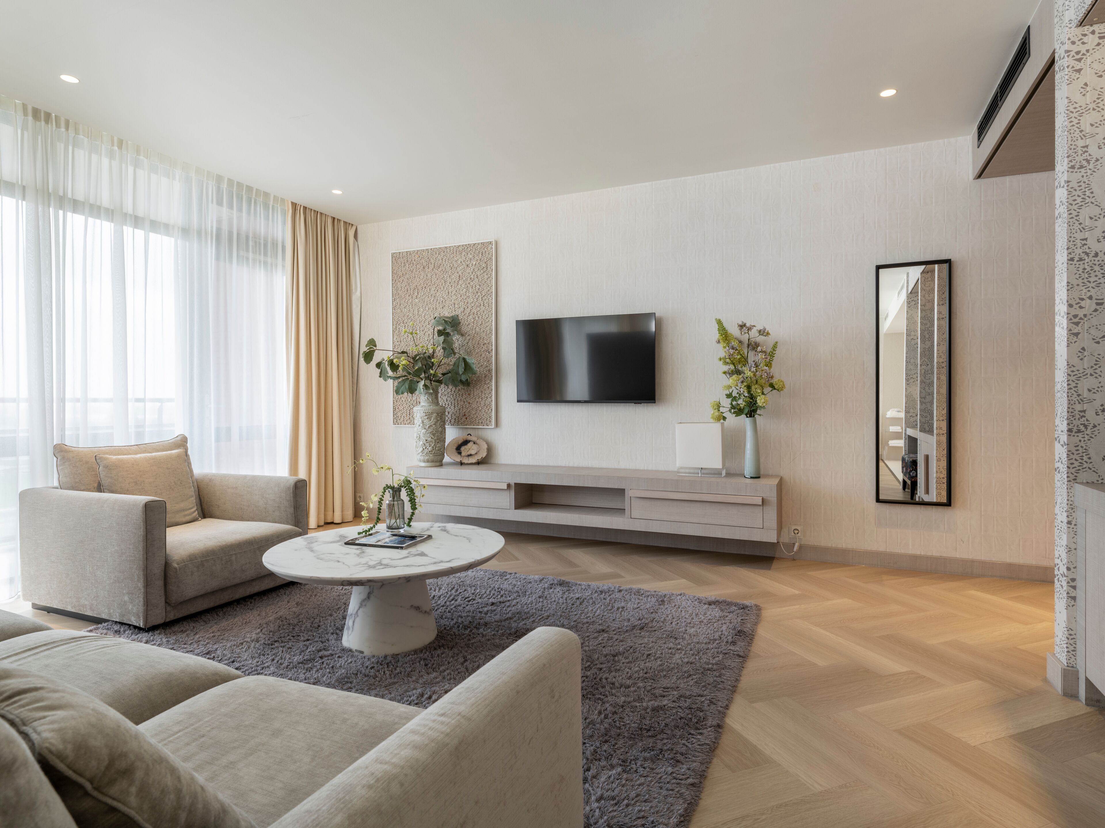 A modern living room with a flat-screen TV mounted on the wall, a grey shag rug, and a beige sofa.