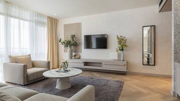 A modern living room with a flat-screen TV mounted on the wall, a grey shag rug, and a beige sofa.