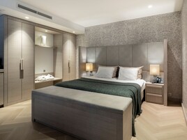 Un dormitorio moderno con una cama grande, un armario, una mesita de noche con lámpara y un cabecero con iluminación integrada.