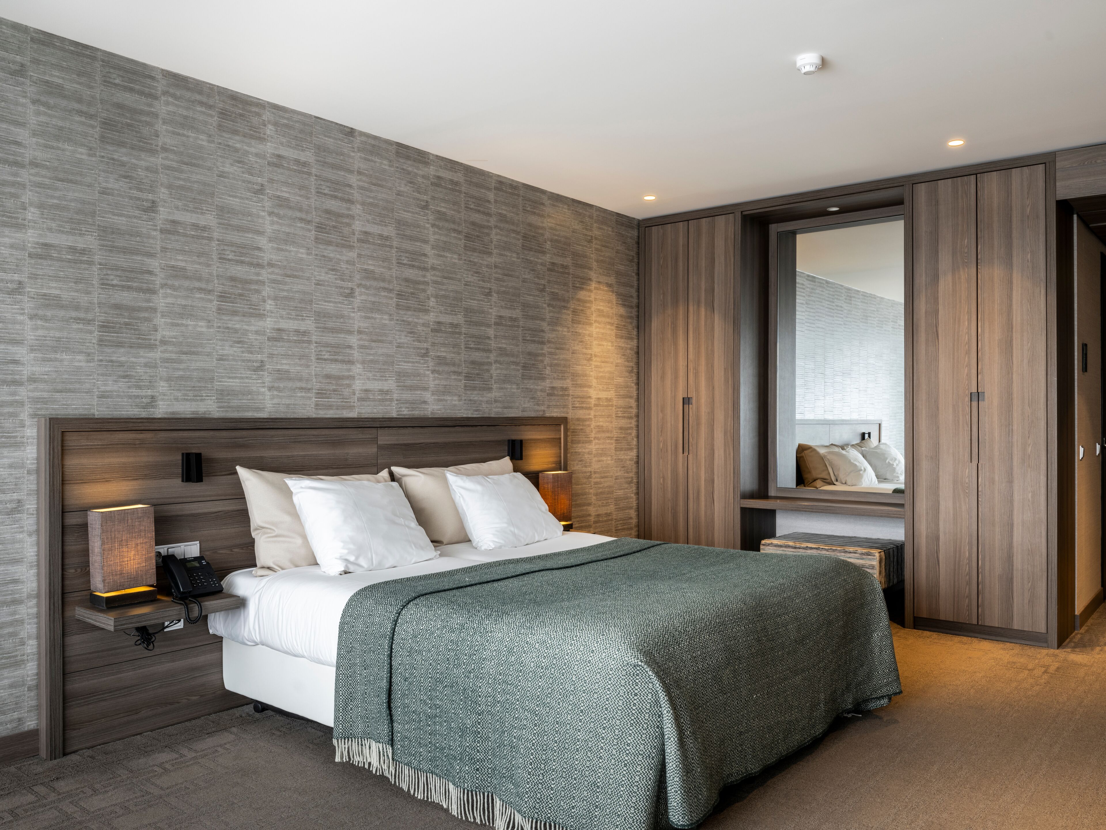 A modern bedroom with a large bed, a nightstand, a bedside lamp, and a wardrobe.