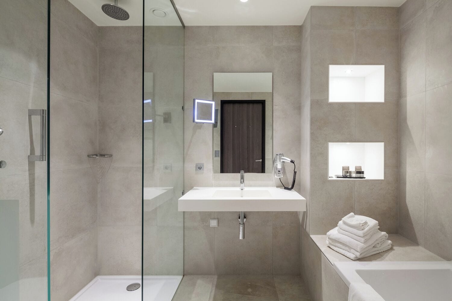 A modern bathroom with a glass-enclosed shower, a large sink with a mirror, and a small shelf with toiletries.