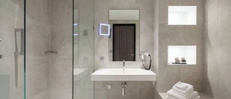 A modern bathroom with a glass-enclosed shower, a large sink with a mirror, and a small shelf with toiletries.