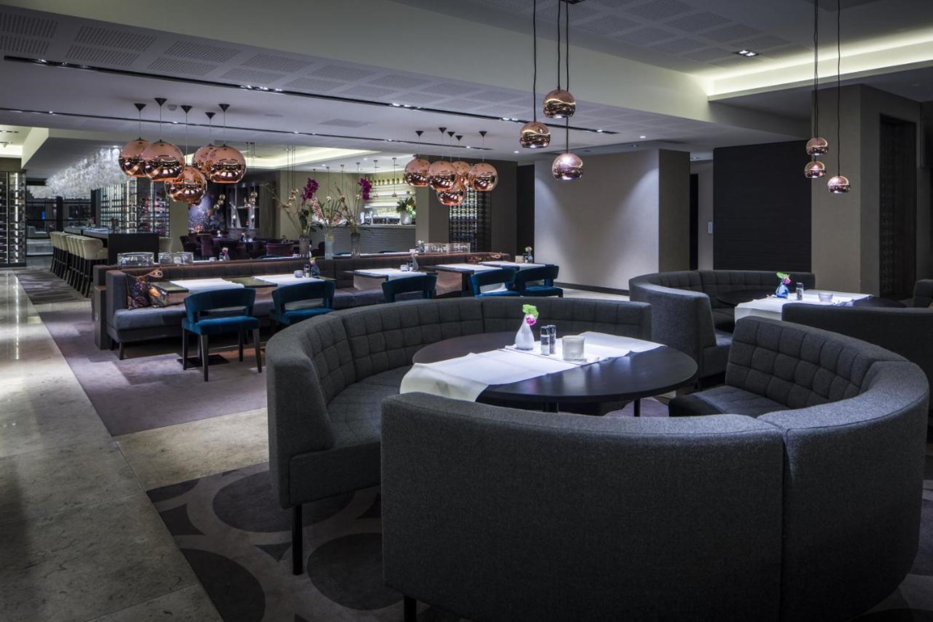 A modern restaurant with round tables and grey upholstered seating.