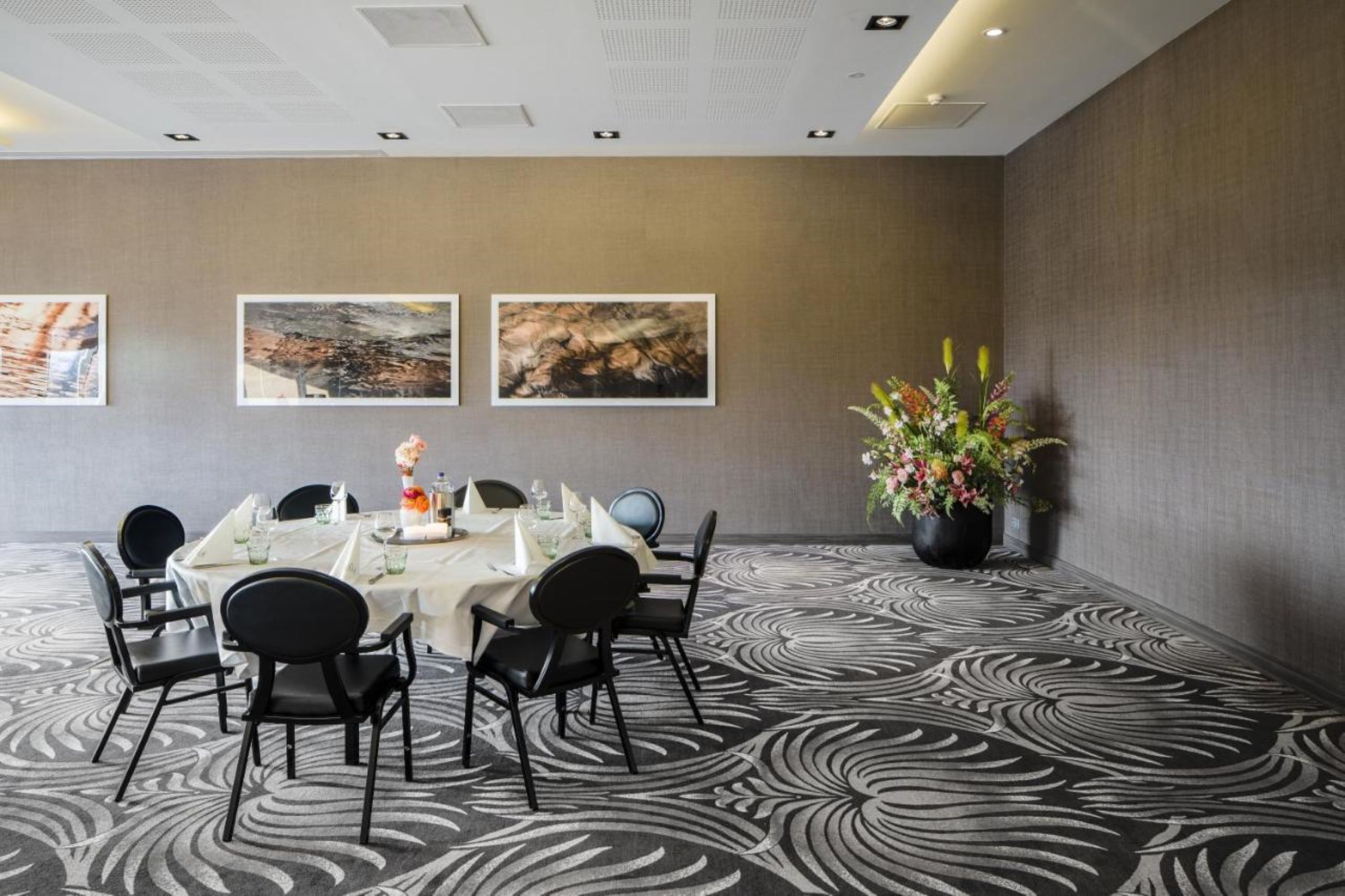Un salón de conferencias con una mesa redonda, sillas negras y obras de arte enmarcadas en la pared.