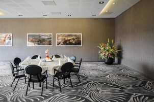 Un salón de conferencias con una mesa redonda, sillas negras y obras de arte enmarcadas en la pared.