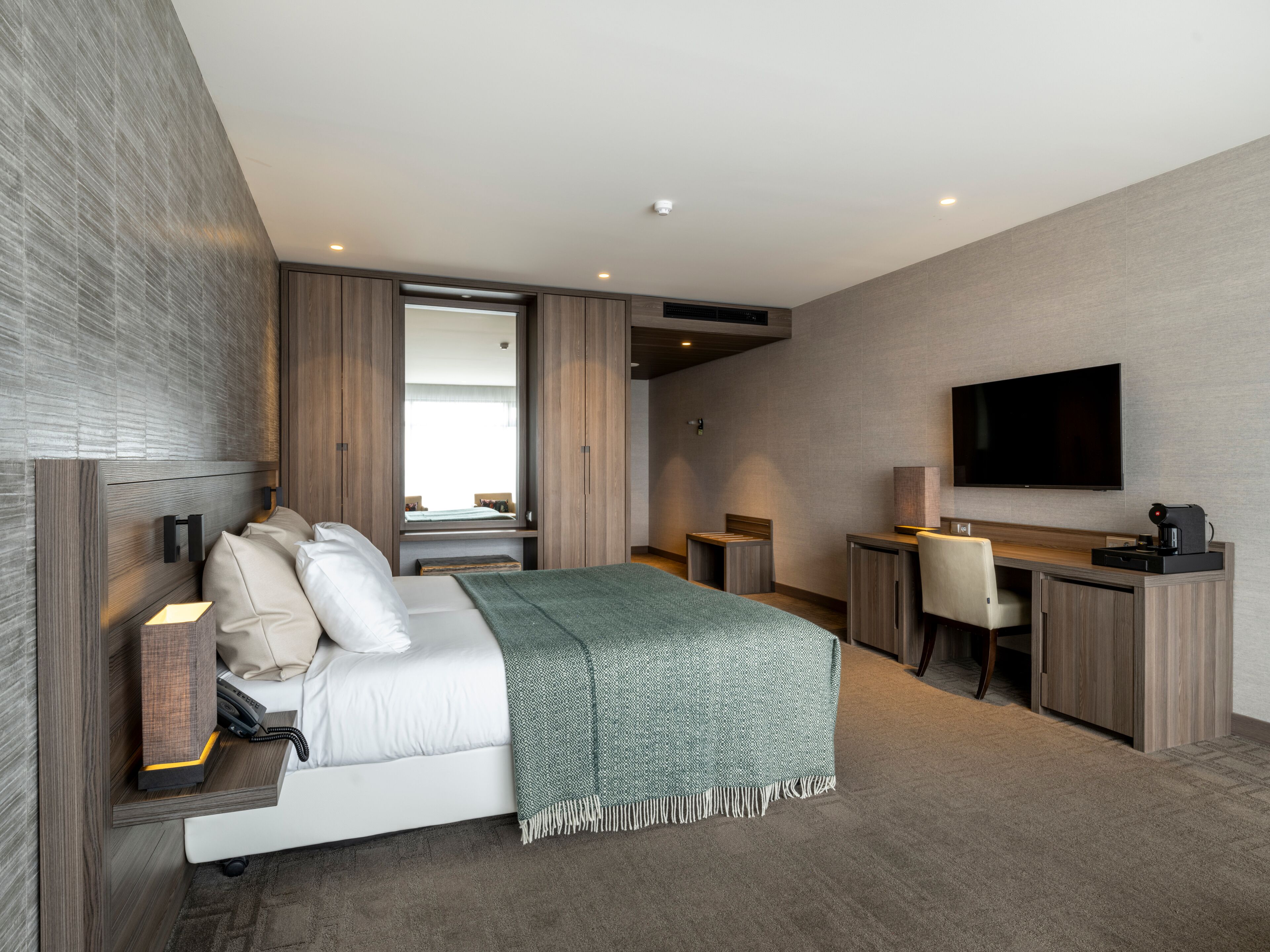 Ein modernes Hotelzimmer mit einem Bett, einem Schreibtisch, einem Stuhl, einem Fernseher und einem großen Fenster.