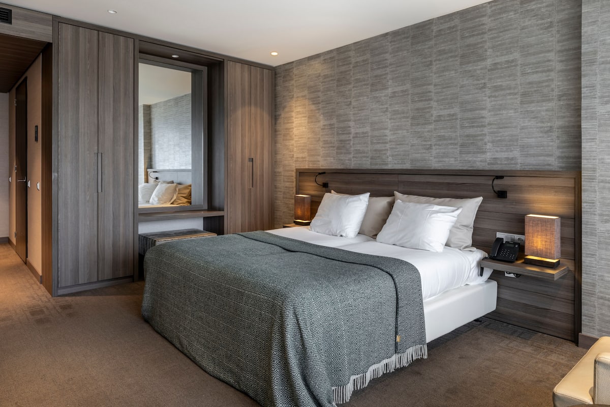 A modern bedroom with a large bed, a wardrobe, a bedside table with a lamp, and a mirror.