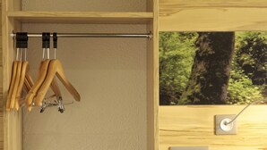 A wooden closet with a hanging rod for clothes, a green bench, and a wall-mounted electrical outlet. - Ibis Styles Sarrebourg Hotel (Sarrebourg)