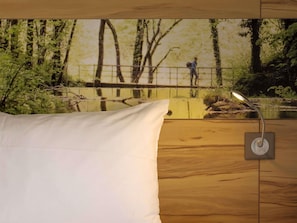 A bedroom with a wooden floor, a white pillow, and a wall-mounted lamp.