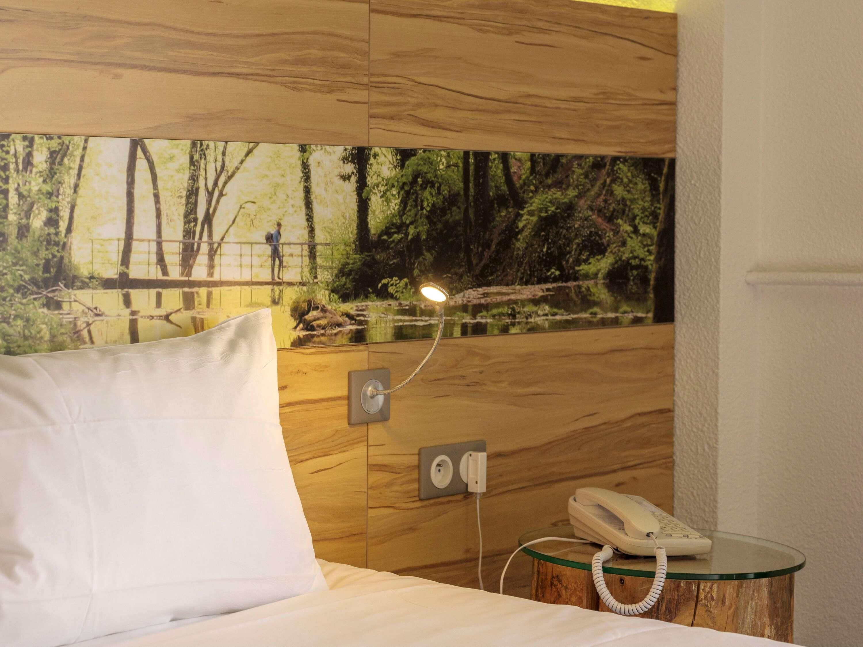Una habitación de hotel con una cama, una mesita de noche con un teléfono y una lámpara fijada a la pared.