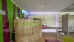 A reception area with a wooden reception desk, a flat-screen TV, and a map on the wall. - Ibis Styles Sarrebourg Hotel (Sarrebourg)