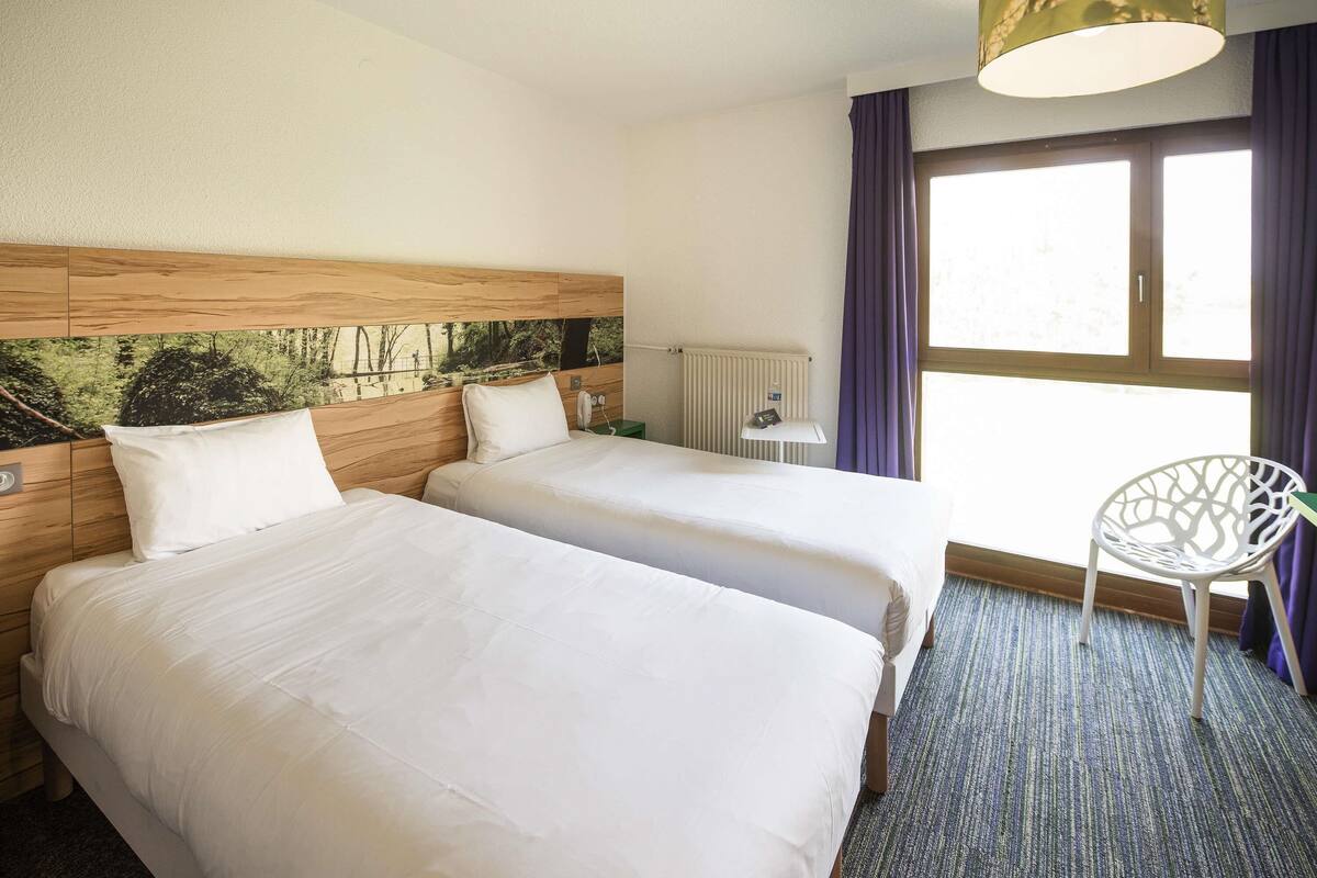 Ein Hotelzimmer mit zwei Betten, einem Heizkörper, einem Fenster mit Vorhängen und einem Sessel.