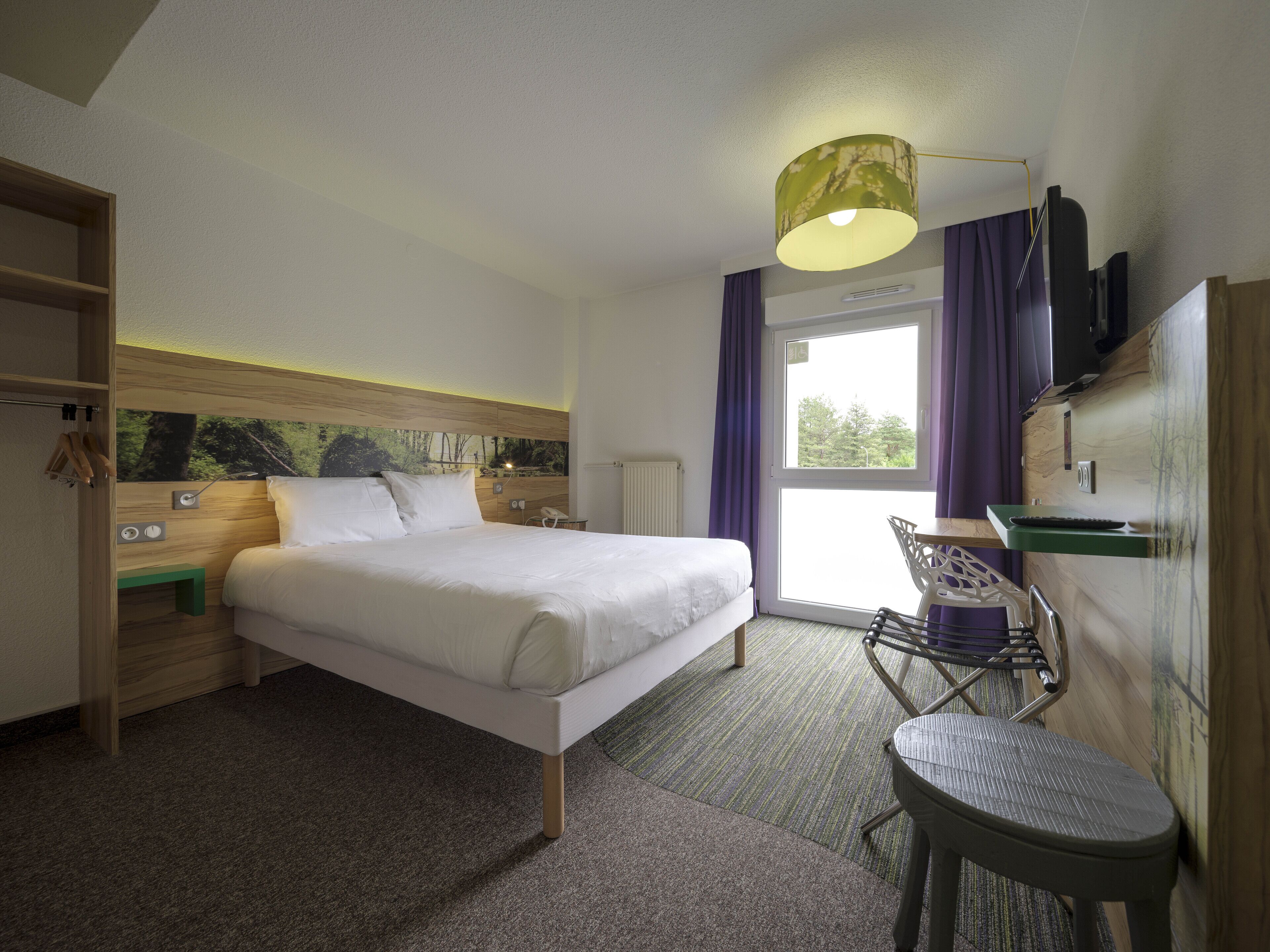 Hotelkamer met een bed, een bureau, een stoel, een kledingkast en een raam met gordijnen.
