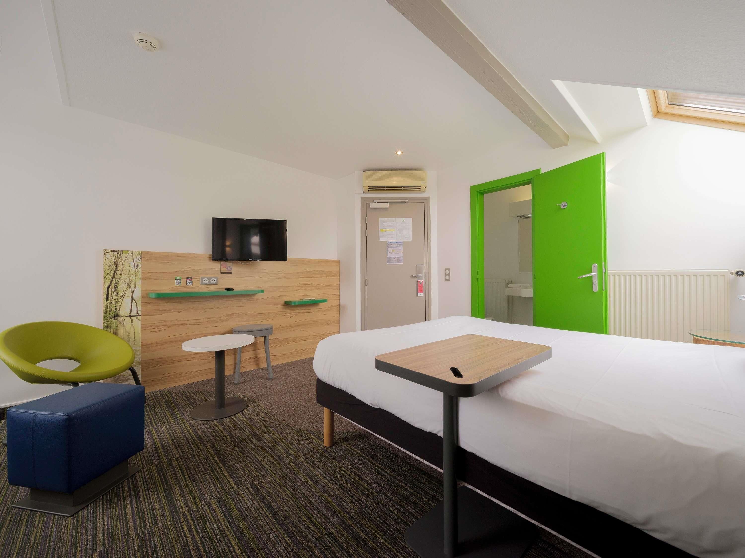 Habitación de hotel con cama, televisión, escritorio, silla y puerta verde.