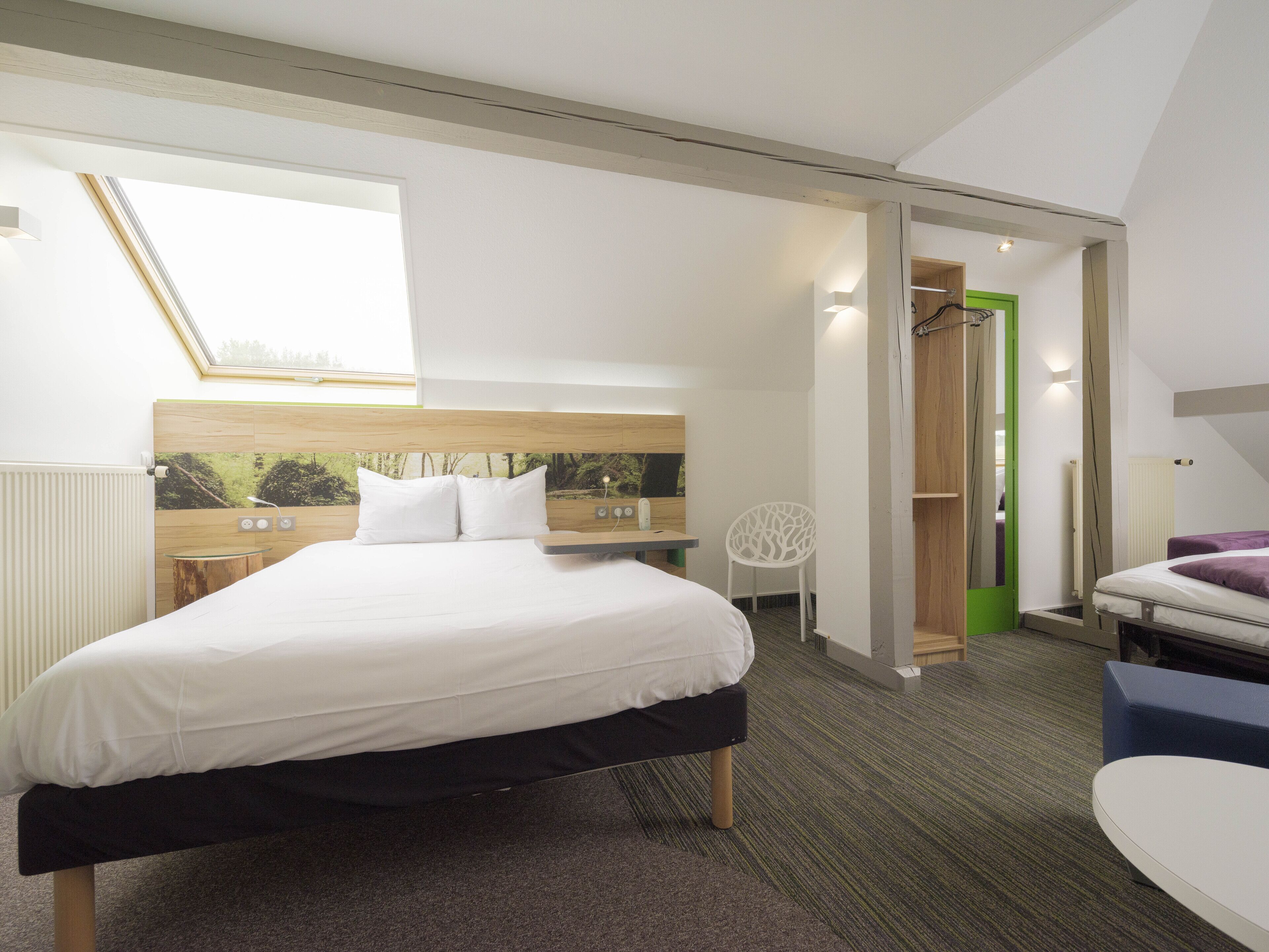 Habitación de hotel moderna con una cama grande, un escritorio pequeño, una silla y vistas al exterior a través de un tragaluz.