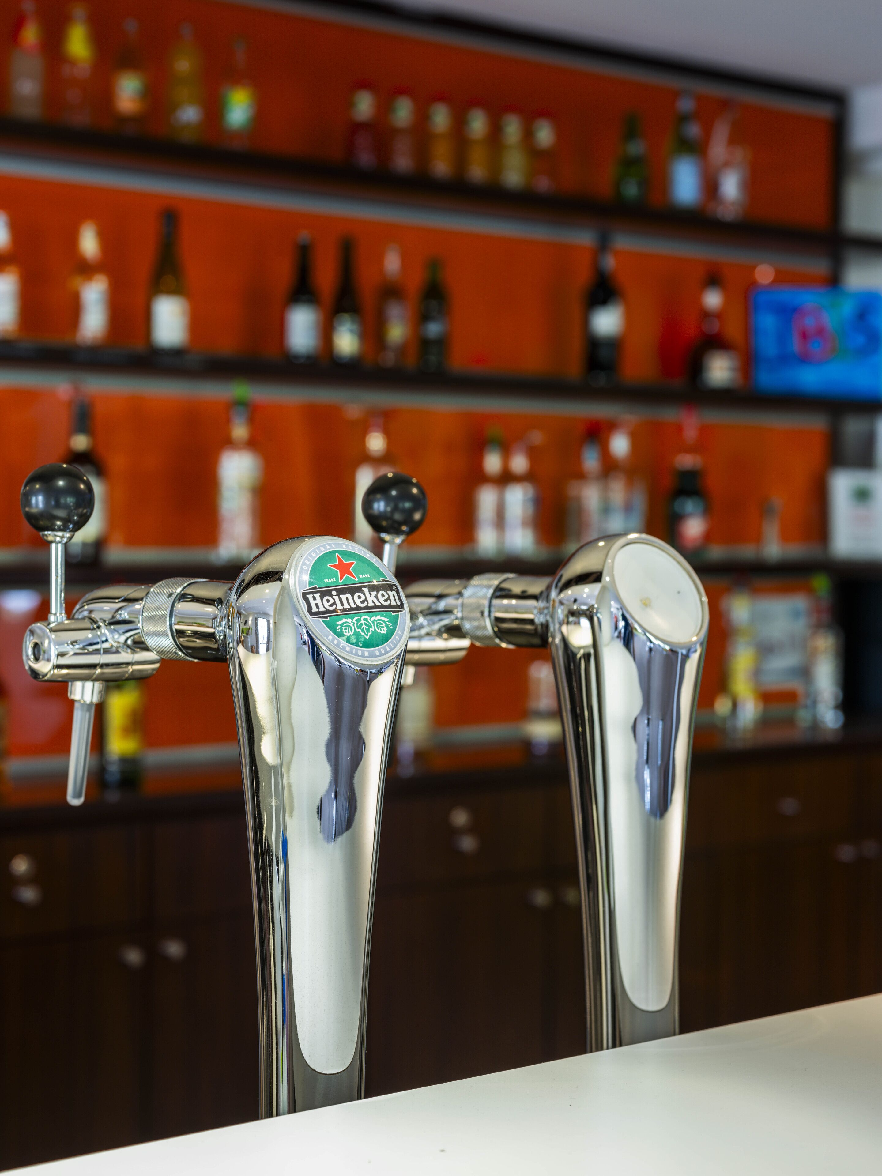 A bar with three Heineken beer taps and shelves of various liquor bottles in the background.