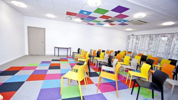 A conference room with colorful checkered carpet, rows of chairs, and a projector screen.