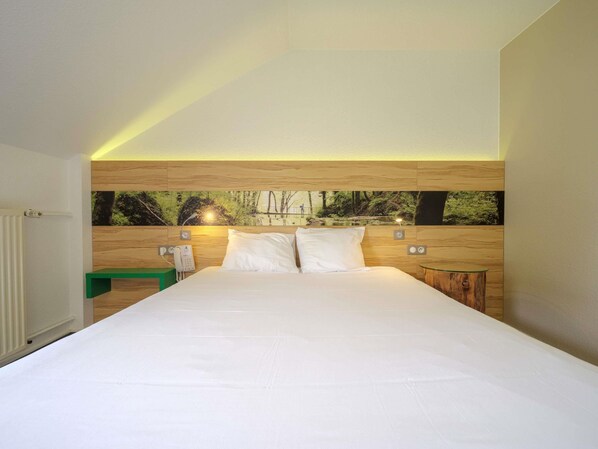 Habitación de hotel moderna con una cama grande, cabecera de madera, mesita de noche verde y una mesita auxiliar de madera, además de un teléfono instalado en la pared.