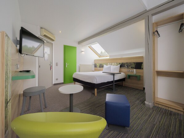 A modern hotel room with a bed, a small table, a green door, a TV, and a window.