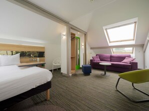 Une chambre d’hôtel moderne avec un lit, un canapé violet, un fauteuil vert et une petite table.