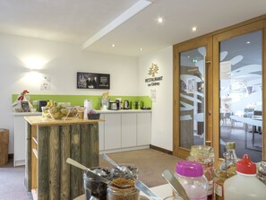 Un restaurant avec un comptoir en bois, un mur vert et une enseigne sur laquelle on peut lire : « RESTAURANT Les Cendres ».