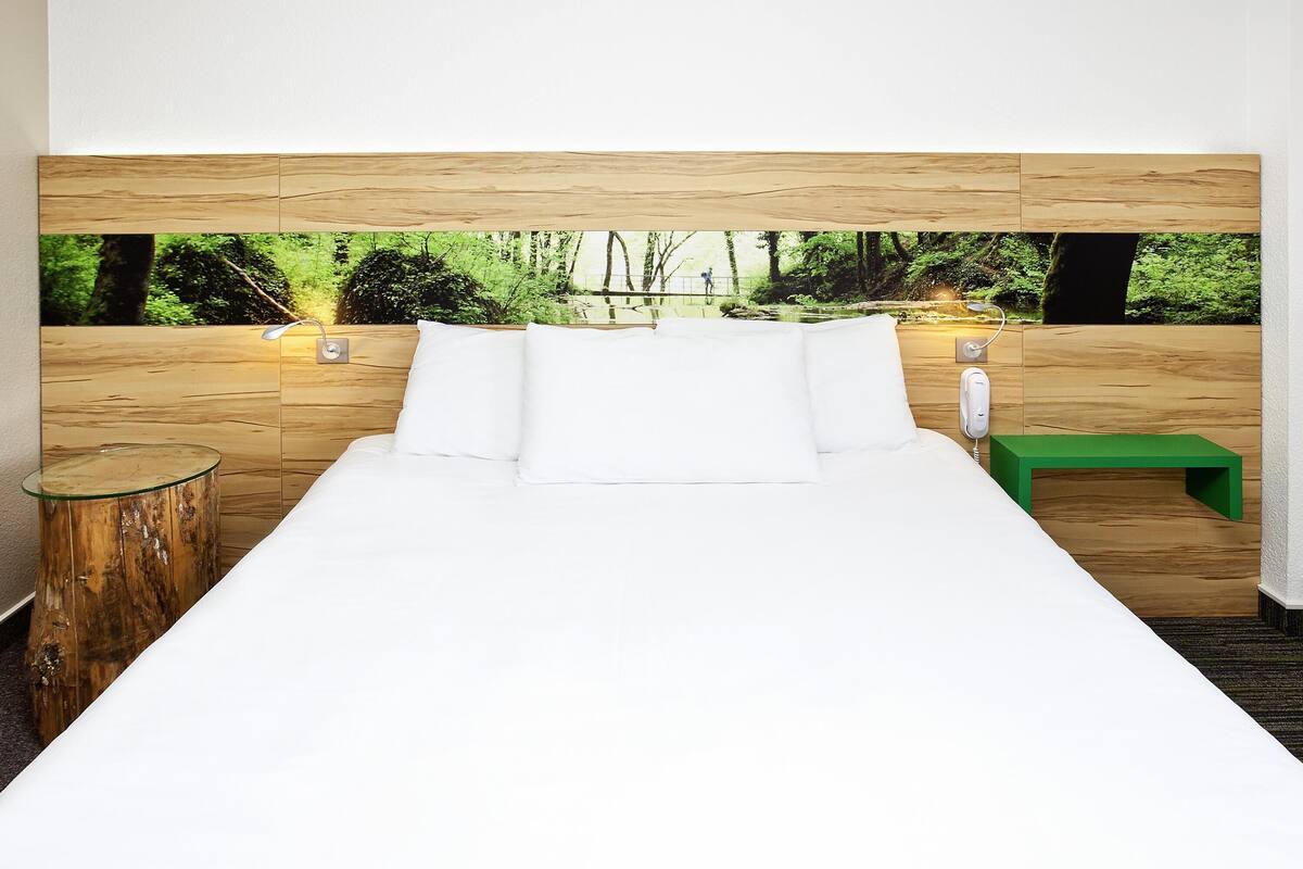 Une chambre à coucher avec un lit, une tête de lit en bois, un banc vert et une table de chevet en bois.