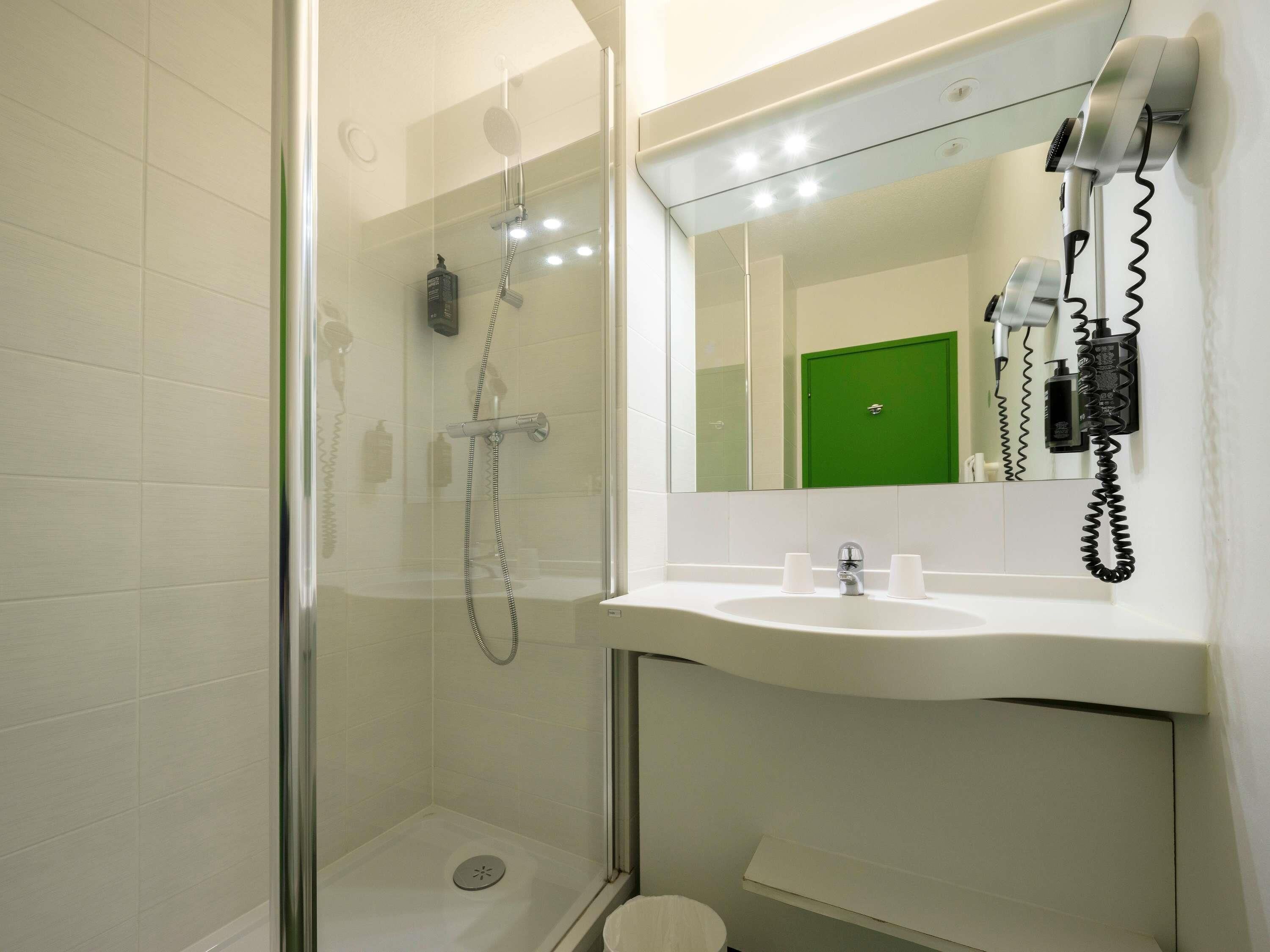 A modern bathroom with a glass-enclosed shower, a white sink with two cups, and a green door in the background.
