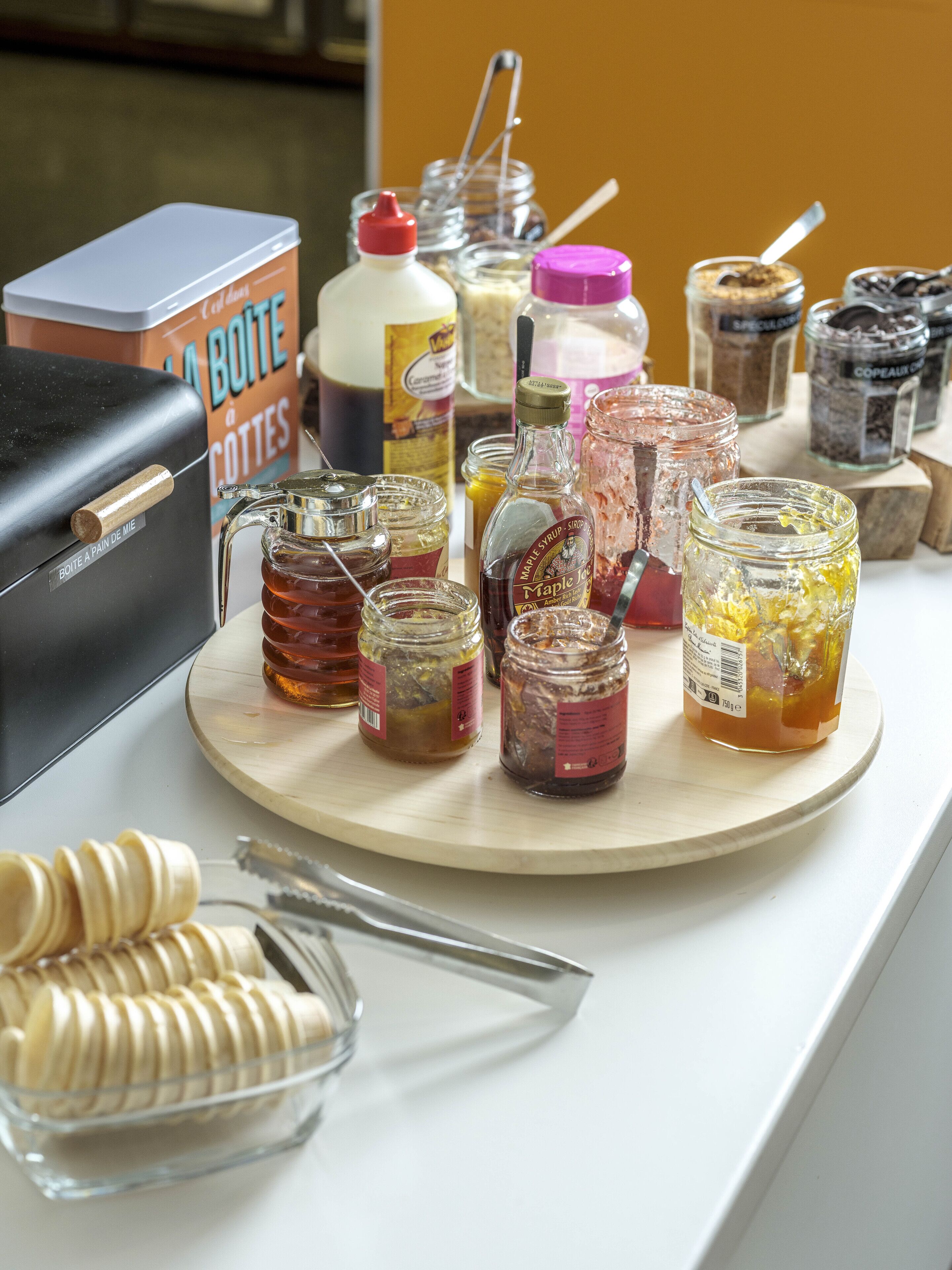 A variety of food items and condiments on a wooden board, including jars of honey, maple syrup, and other preserves.