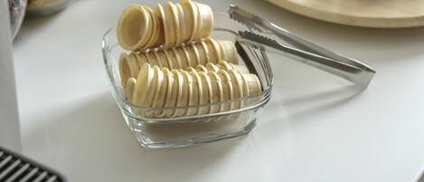 Una encimera de cocina con frascos de condimentos, una caja de azúcar y un bol de vidrio con rebanadas de pan.