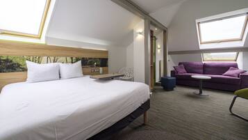 A modern hotel room with a large bed, a purple sofa, a small table, and a chair.