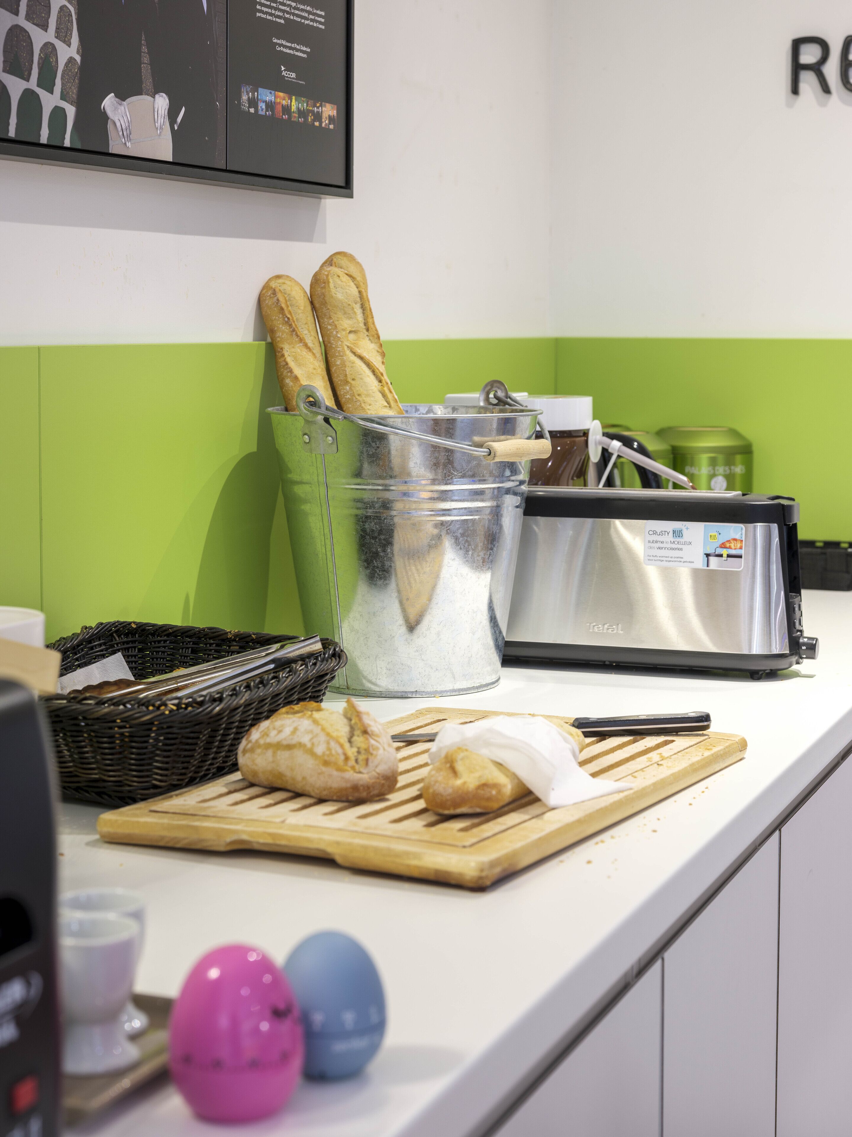 Una encimera de cocina con un tostador, una cesta de pan, una tabla de cortar con pan y una pared verde.