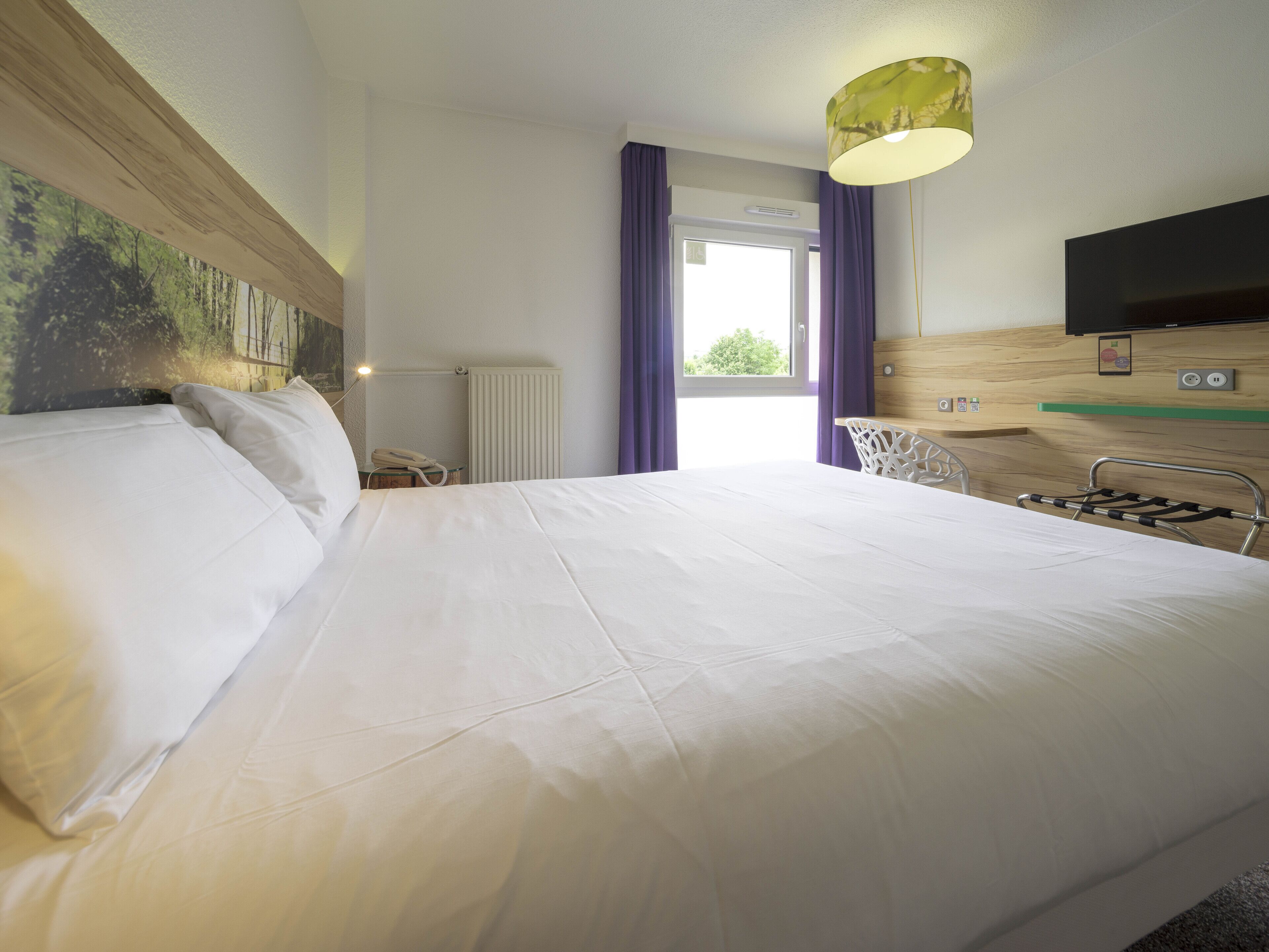 Une chambre d’hôtel avec un grand lit, un bureau, une chaise, une télévision et une fenêtre avec des rideaux.