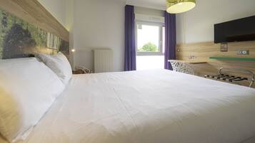Une chambre d’hôtel avec un grand lit, un bureau, une chaise, une télévision et une fenêtre avec des rideaux.