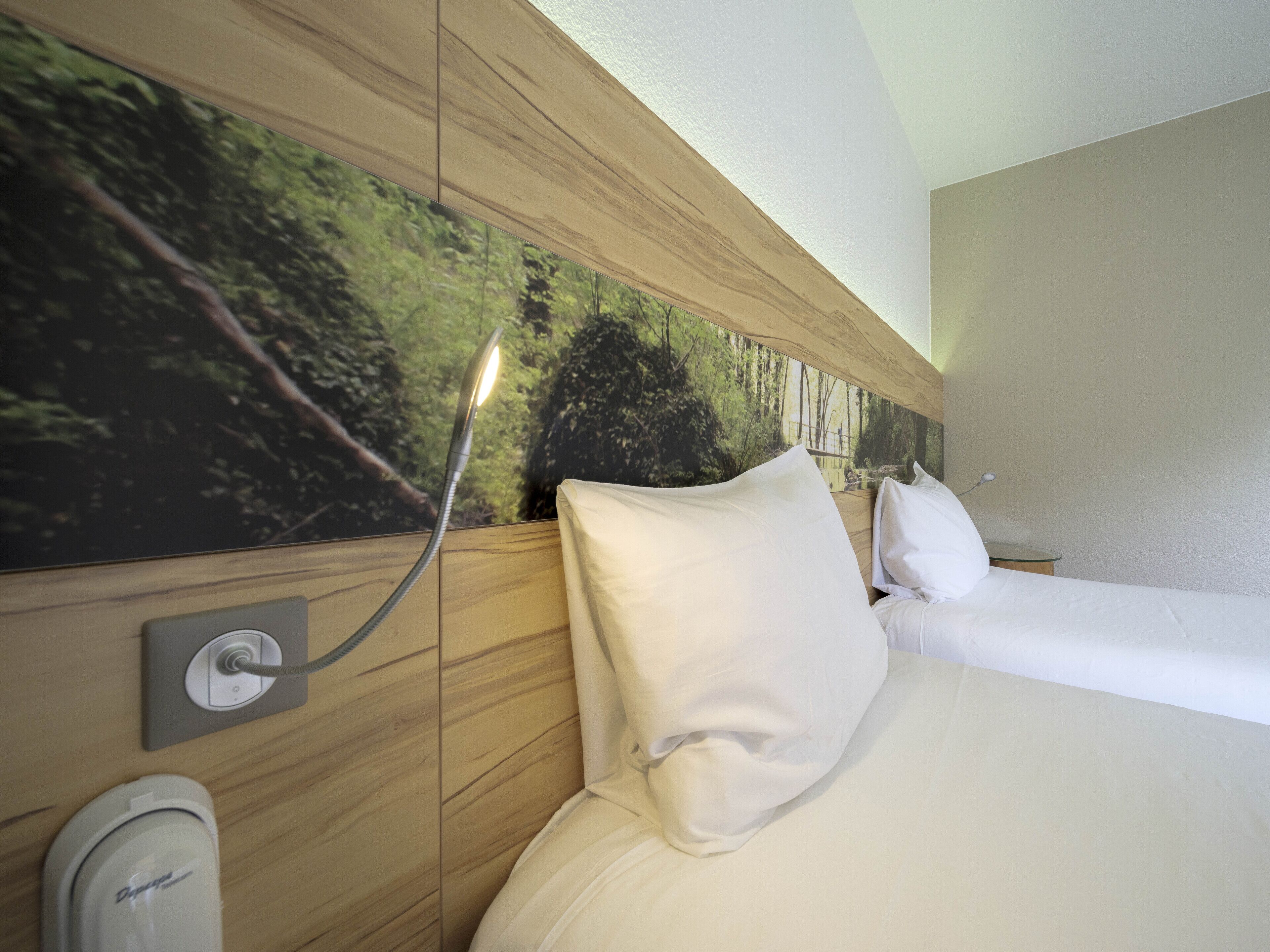 A hotel room with a bed, a nightstand, a lamp, and a wall-mounted power outlet.