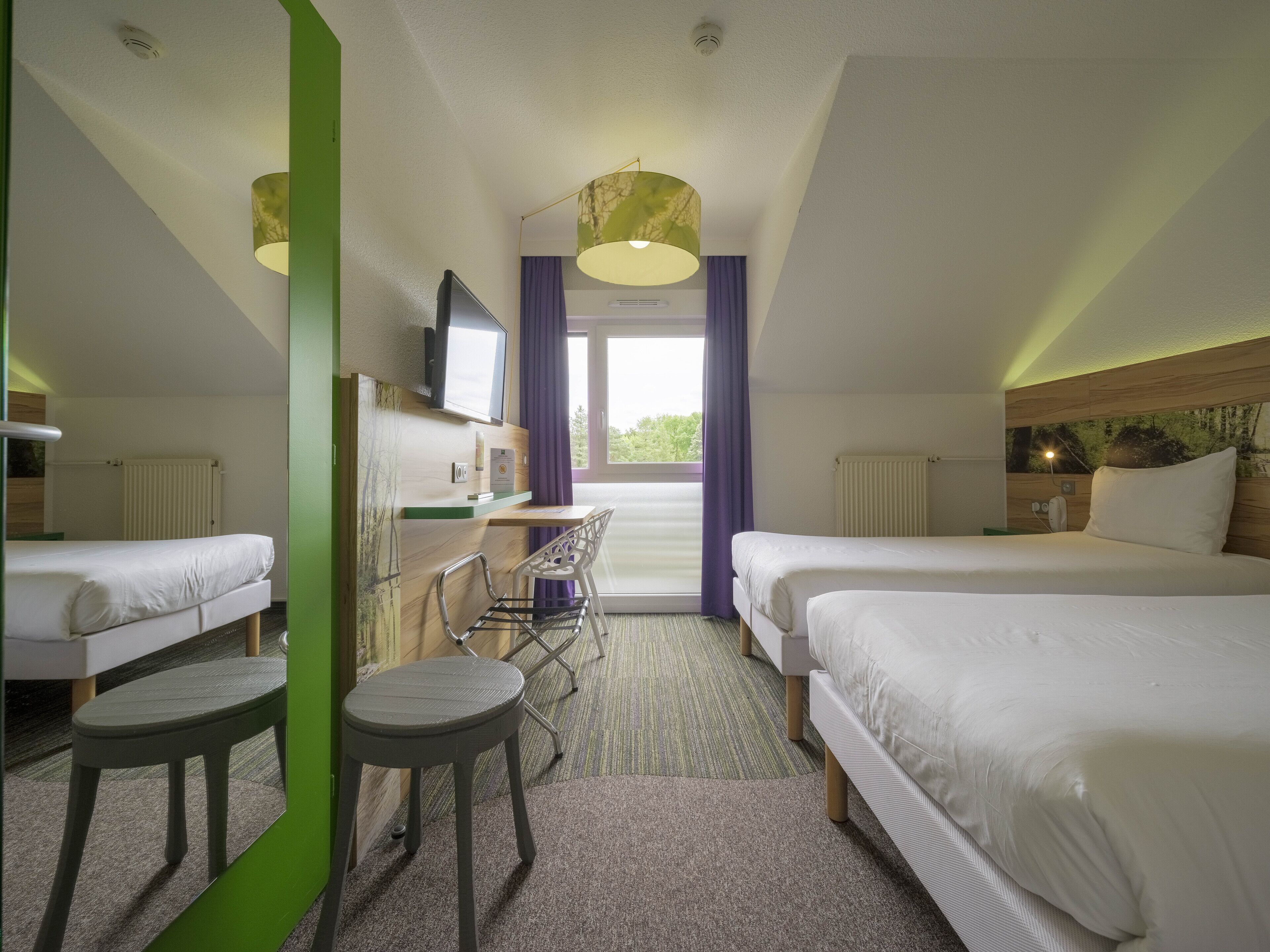 A hotel room with two beds, a desk, a chair, and a TV.