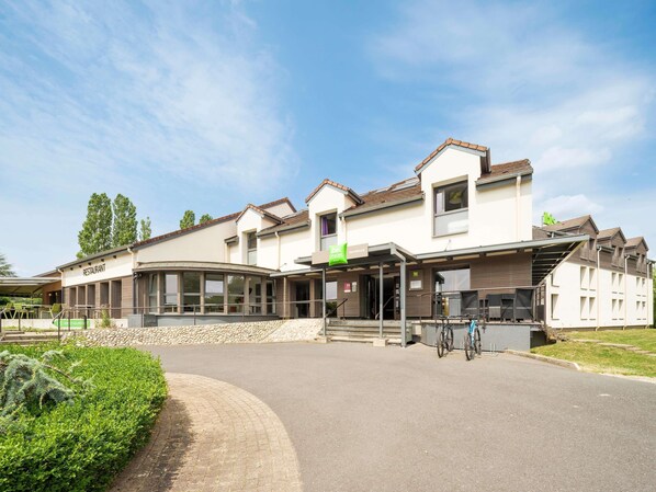 A modern building with a restaurant on the ground floor, a covered outdoor seating area, and a bike parking area.