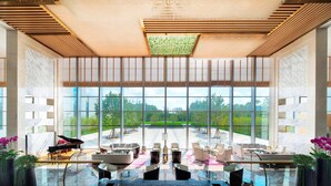 Un lobby espacioso con un piano de cola, asientos modernos y amplias ventanas que ofrecen vistas al exterior.