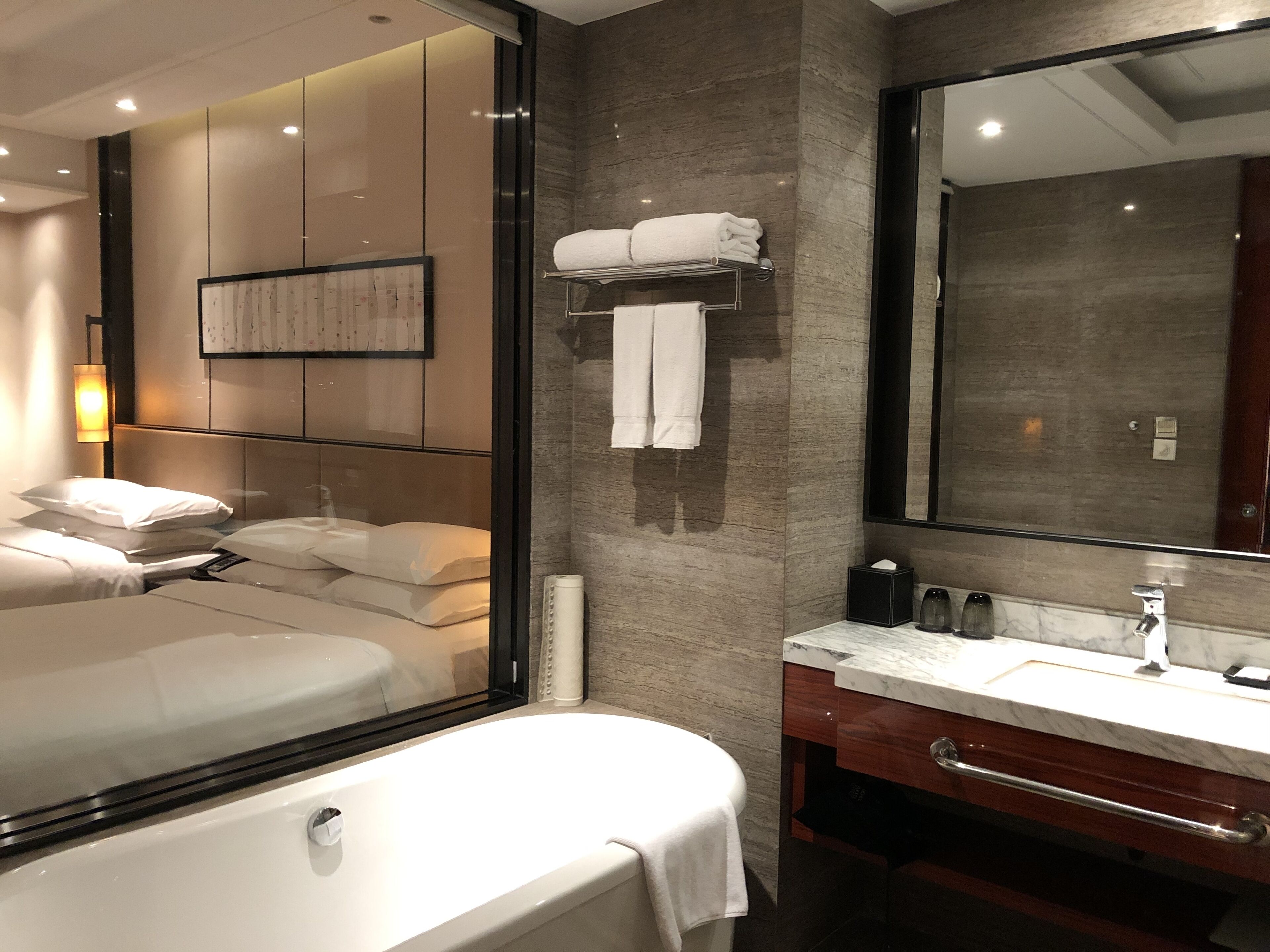 A modern hotel room with a large bed, a separate bathroom with a marble countertop, and a large mirror.