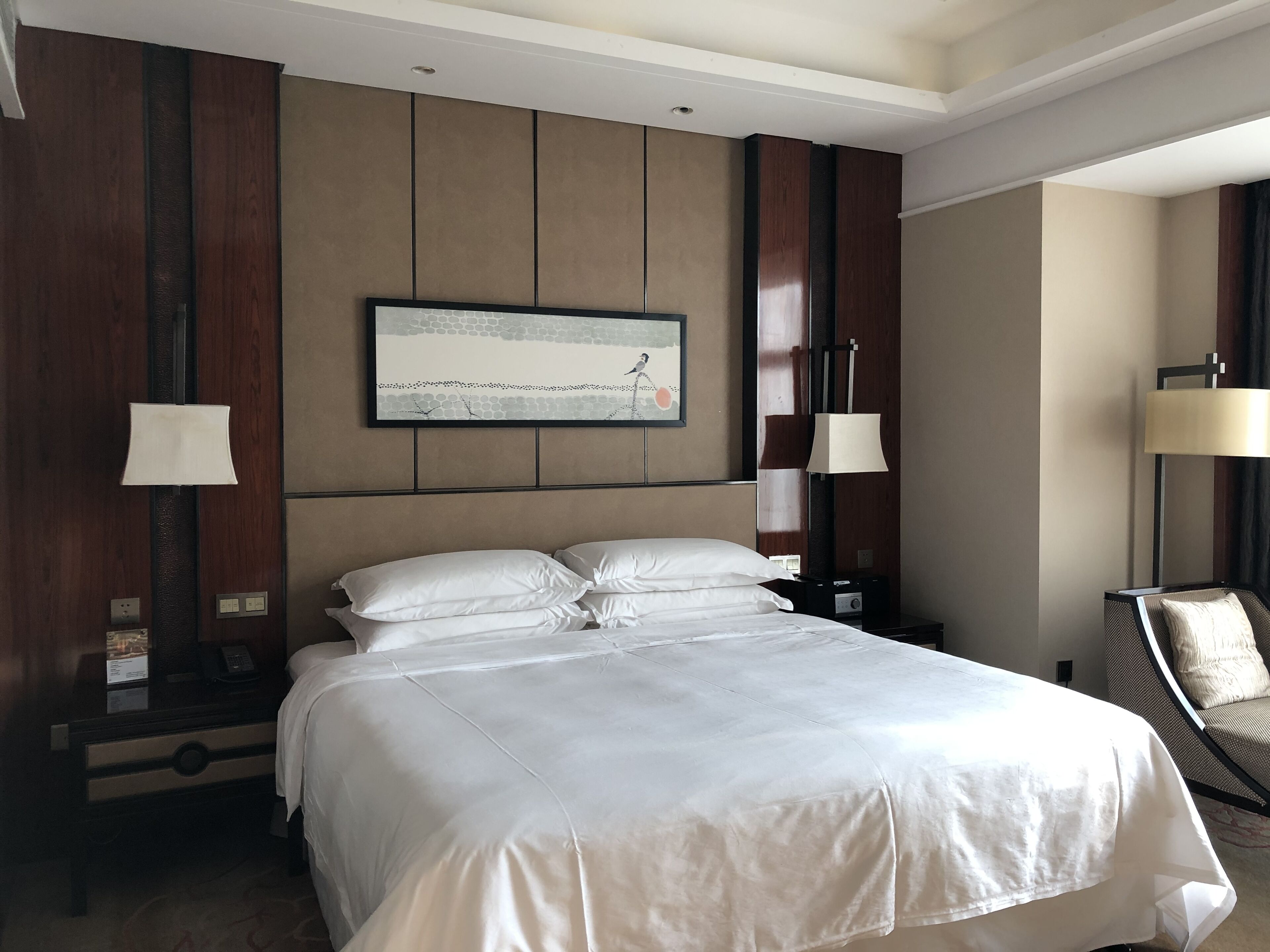 Una habitación de hotel con una cama grande, dos mesitas de noche, una silla y una obra de arte en la pared.