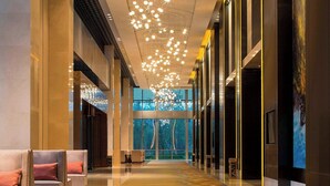 Un moderno vestíbulo de hotel con un largo pasillo, zonas de estar e iluminación colgante en el techo.