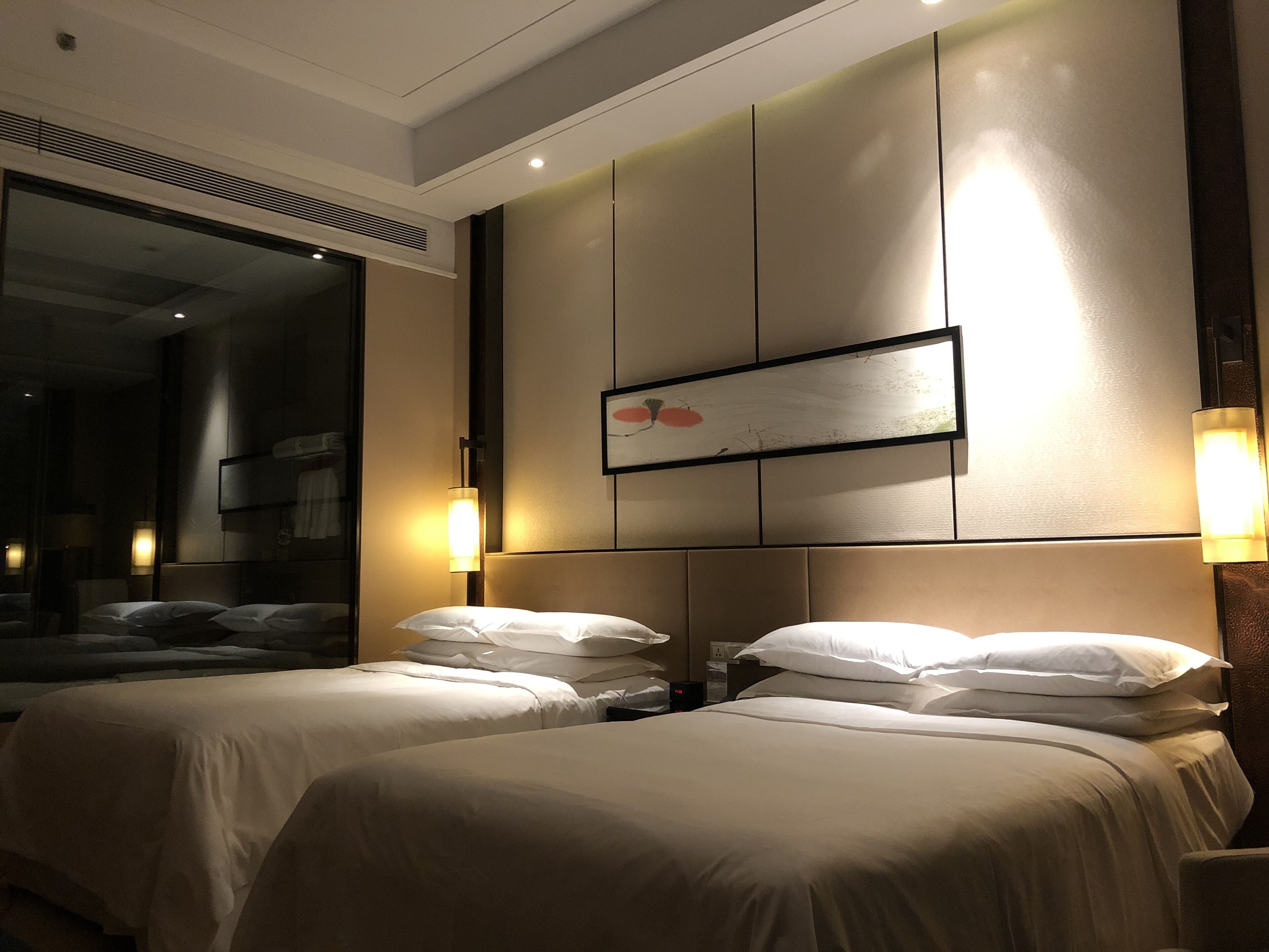 A hotel room with two beds, a large mirror, wall-mounted artwork, and bedside lamps.