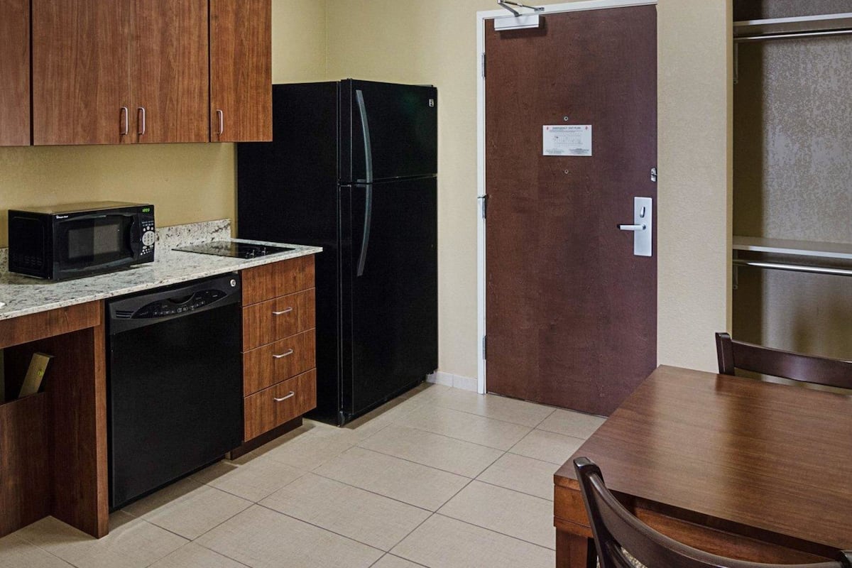 A compact kitchen with wooden cabinets, a black refrigerator, a microwave, and a small dishwasher.