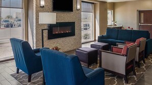 A modern hotel lobby with a stone fireplace, comfortable seating, a flat-screen TV, and large windows offering a view of the parking lot. - Comfort Inn Midland South I-20 (Midland)