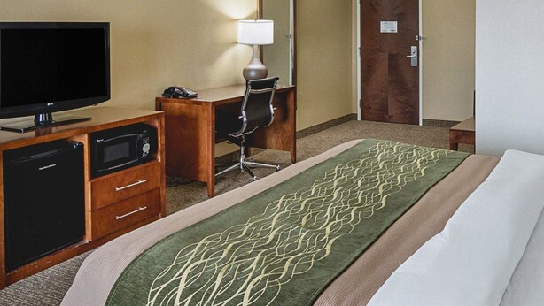 Une chambre d’hôtel équipée d’un lit, d’un bureau avec un ordinateur, d’une télévision, d’un four à micro-ondes et d’une porte.