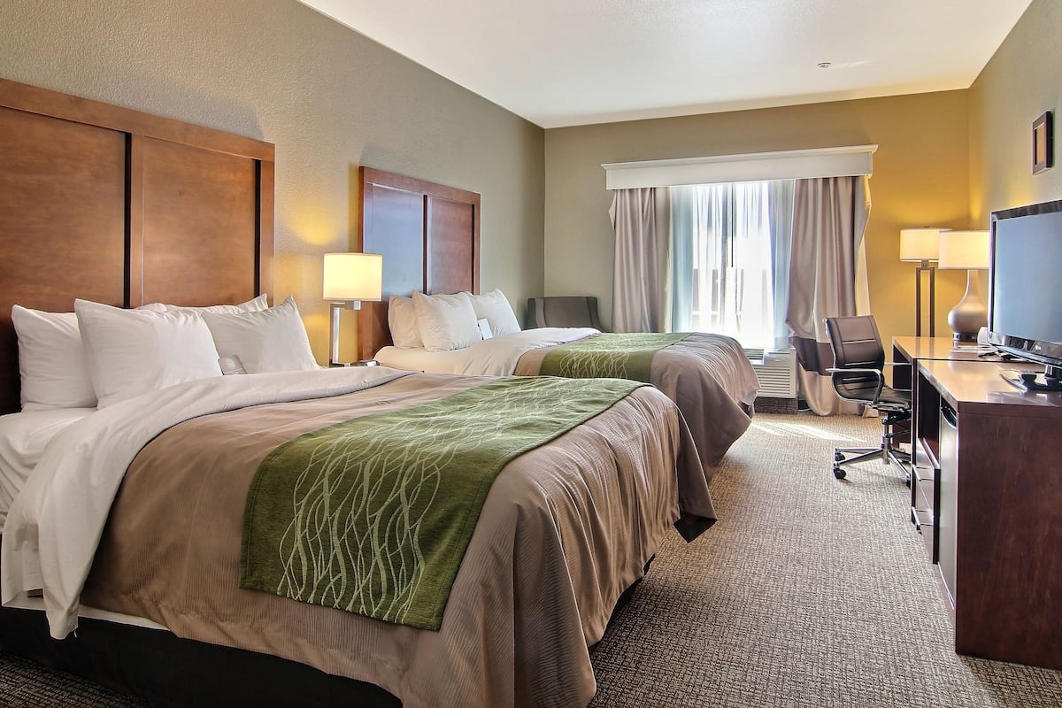 A hotel room with two beds, a desk, a chair, and a television.