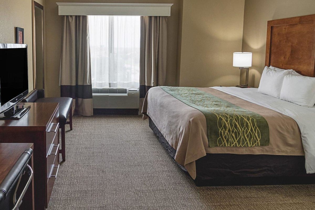 A hotel room with a bed, a desk, a television, a lamp, and a window with curtains.